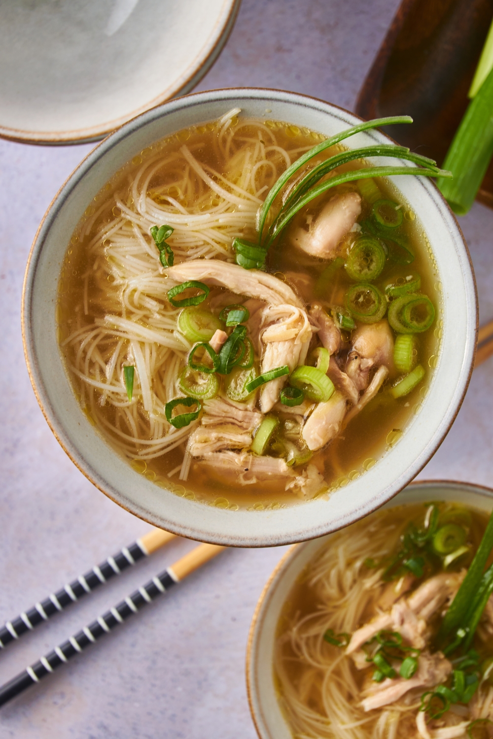 Overhead view of shredded chicken in broth with rice noodles and diced green onions. There is a second bowl of chicken soup next to it.