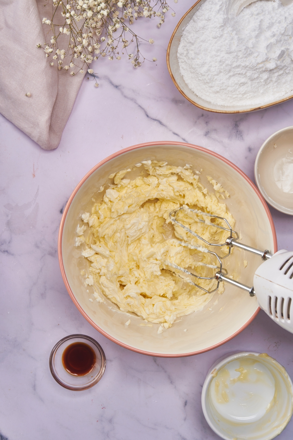 A bowl with cream cheese and butter whisked together using an electric hand mixer.