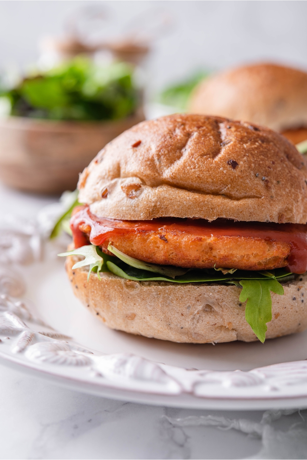 Close up of a salmon burger with ketchup dripping down the side of the salmon patty and lettuce beneath it.