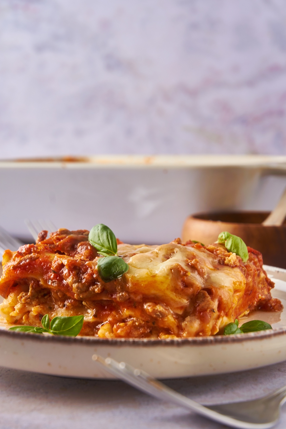 Close up of a slice of lasagna layered with meat sauce, melted cheese, and a garnish of fresh basil.