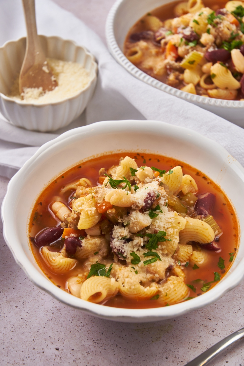 A serving of pasta e fagioli soup garnished with parmesan cheese and fresh green herbs.