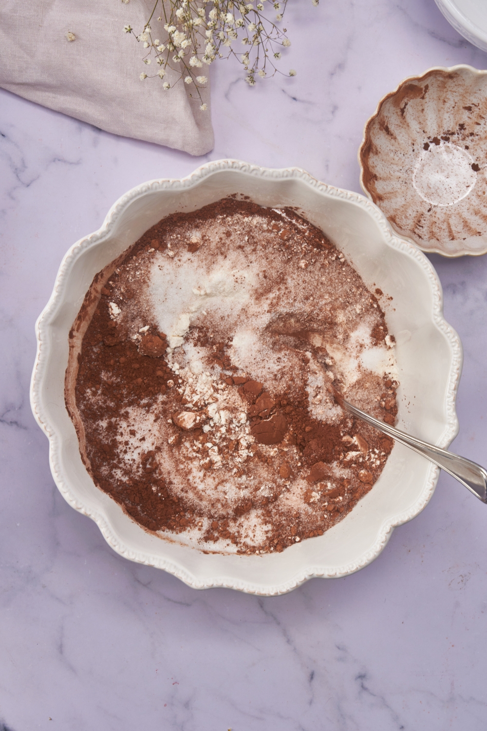 A white mixing bowl with flour, sugar, and cocoa powder added but not fully mixed together.
