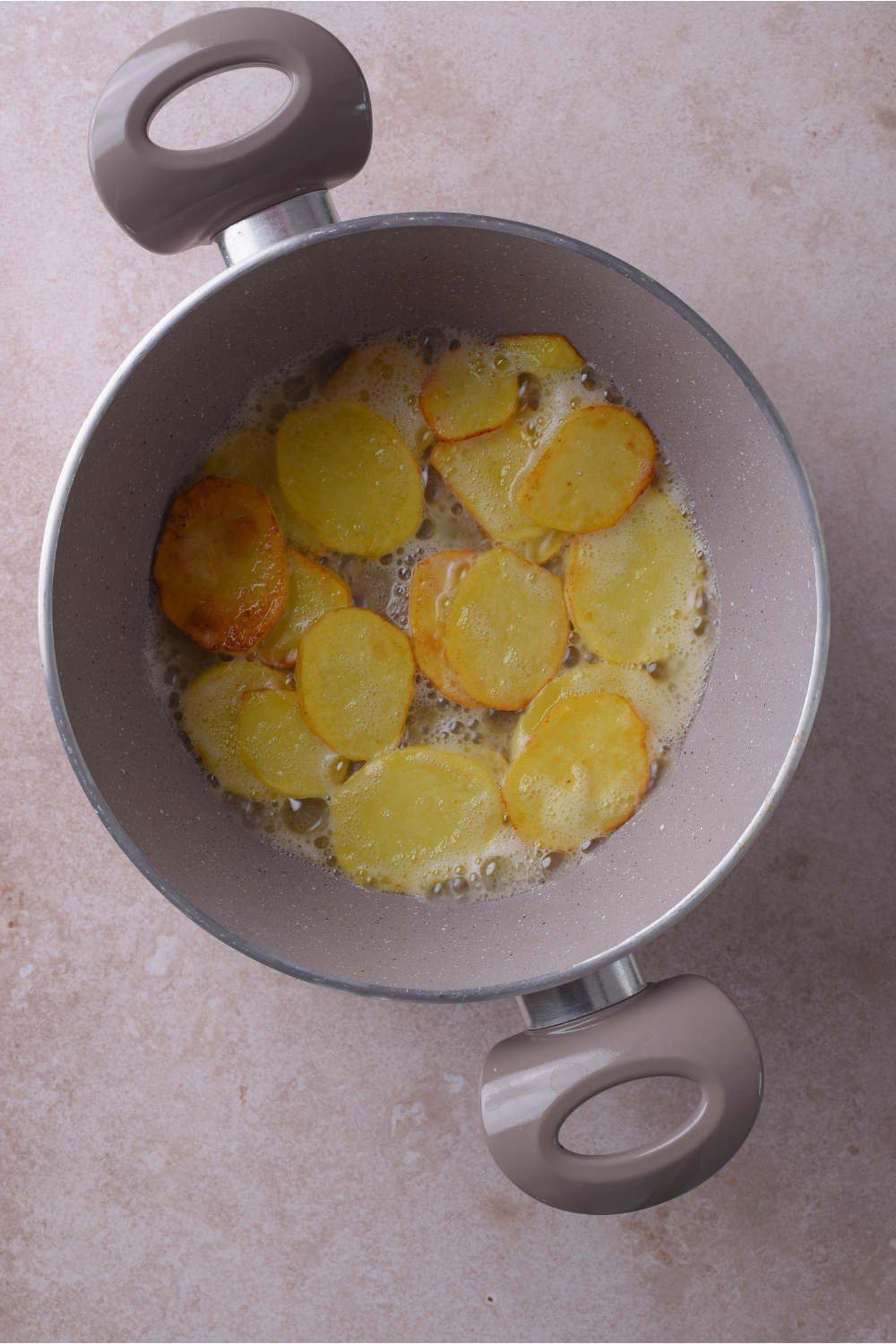 A large grey pot with thinly sliced potatoes frying in butter.