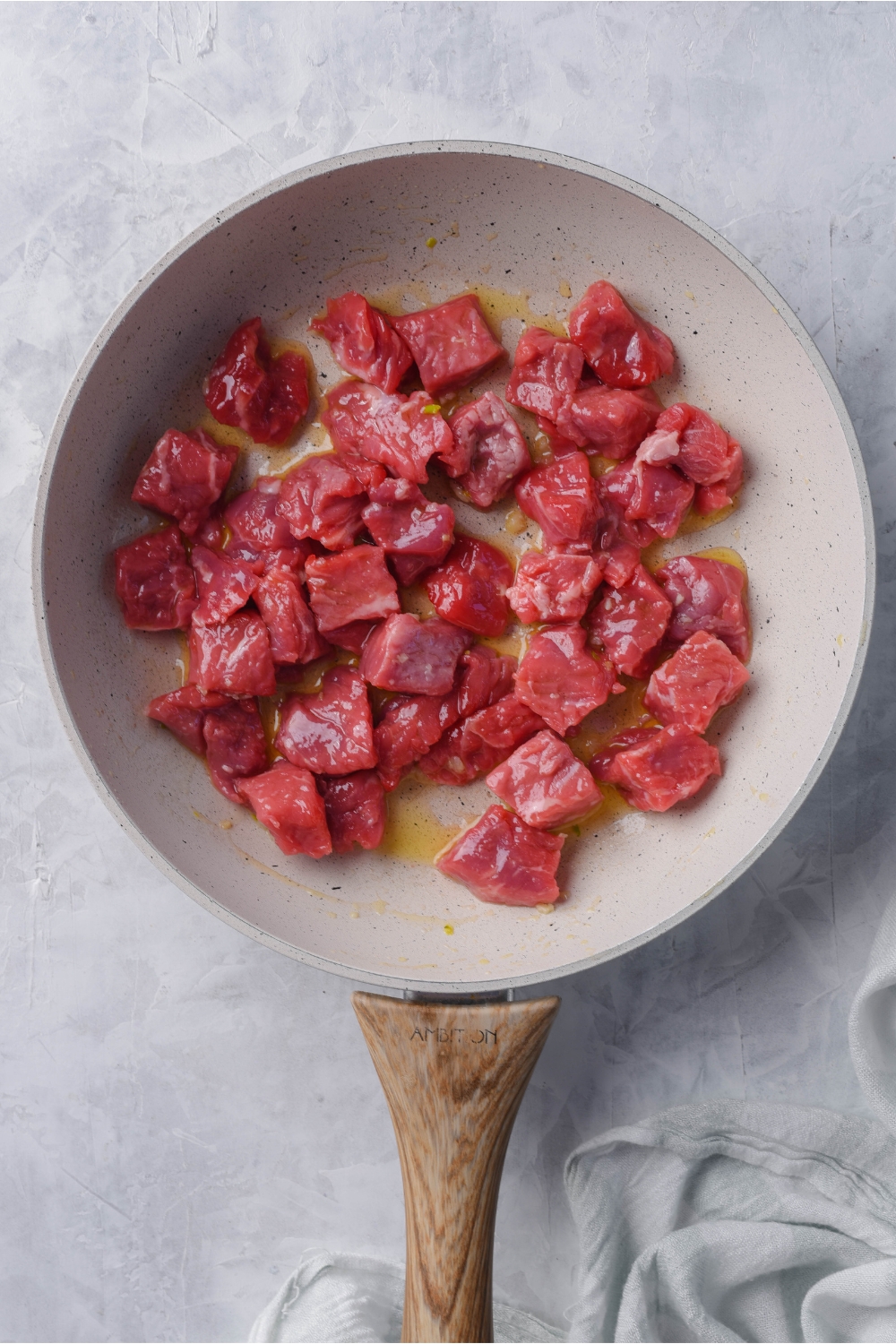 A grey skillet with cubes of raw steak cooking in butter.