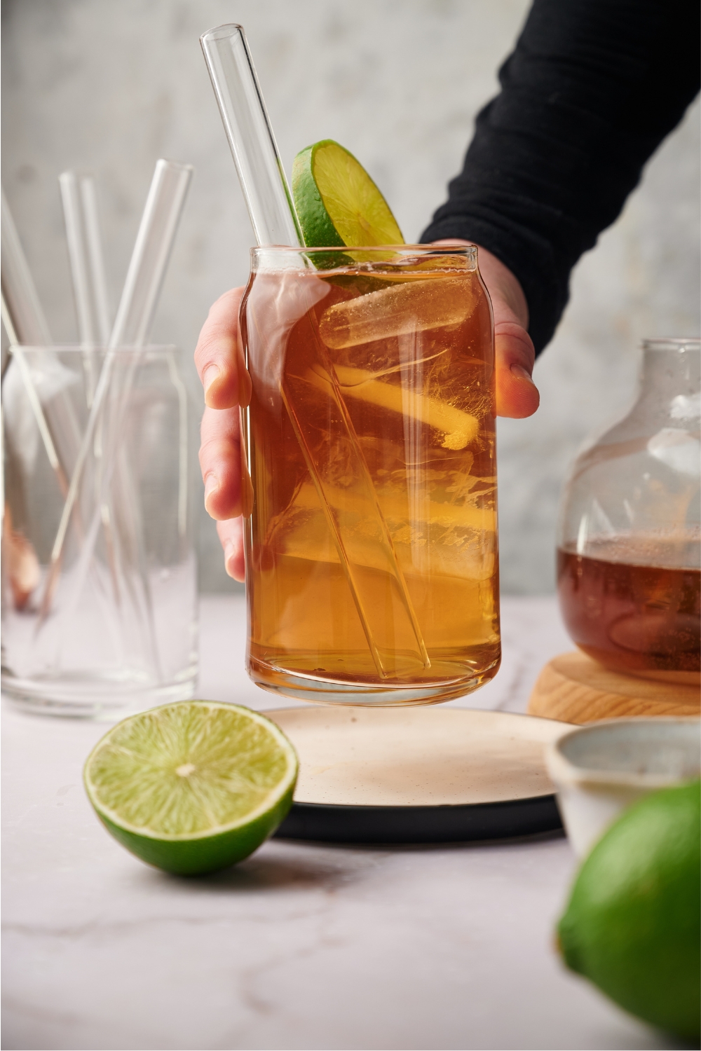 A hand grabbing a glass of iced tea off a plate. The glass has a straw and a lime wedge in it.