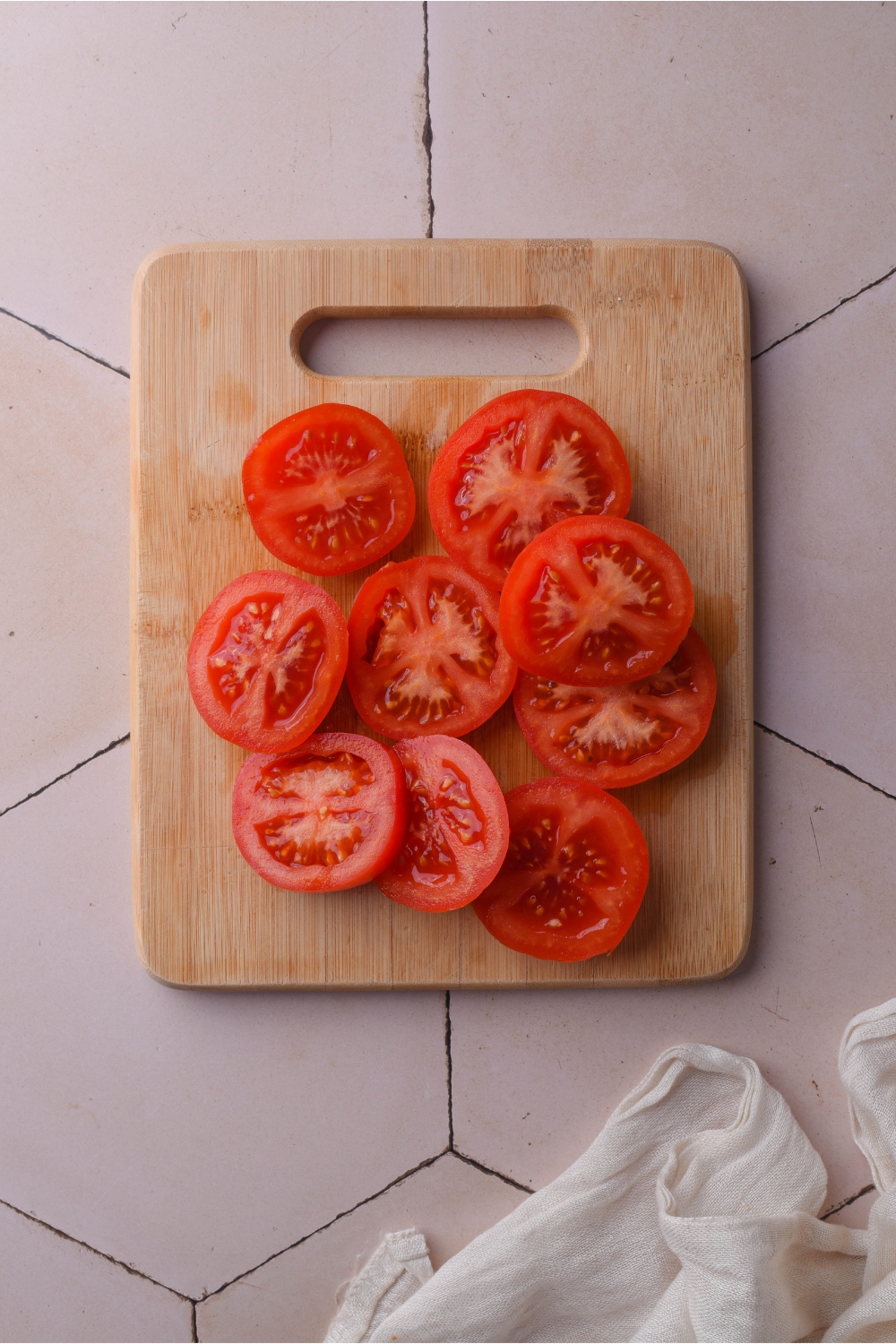 Overhead view of a pile of tomato slices on a wooden cutting board.