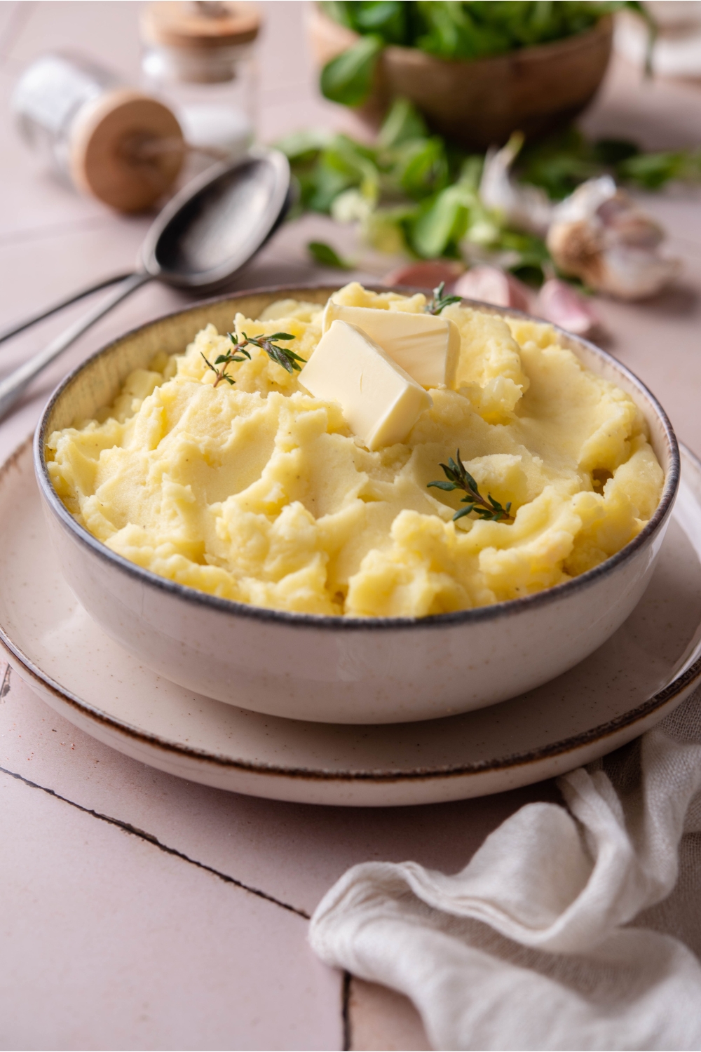 A bowl of mashed potatoes with two tabs of butter and fresh green herbs garnished on top.
