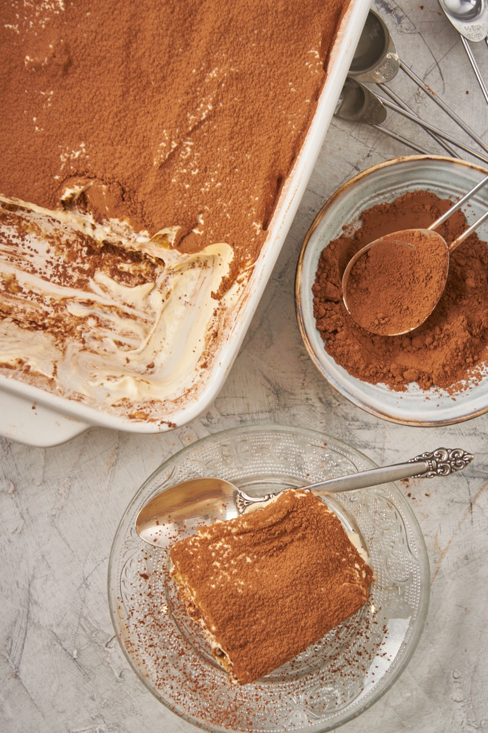 An overhead view of a slice of tiramisu on a plate. The remaining tiramisu is in the pan to the side of the plate.