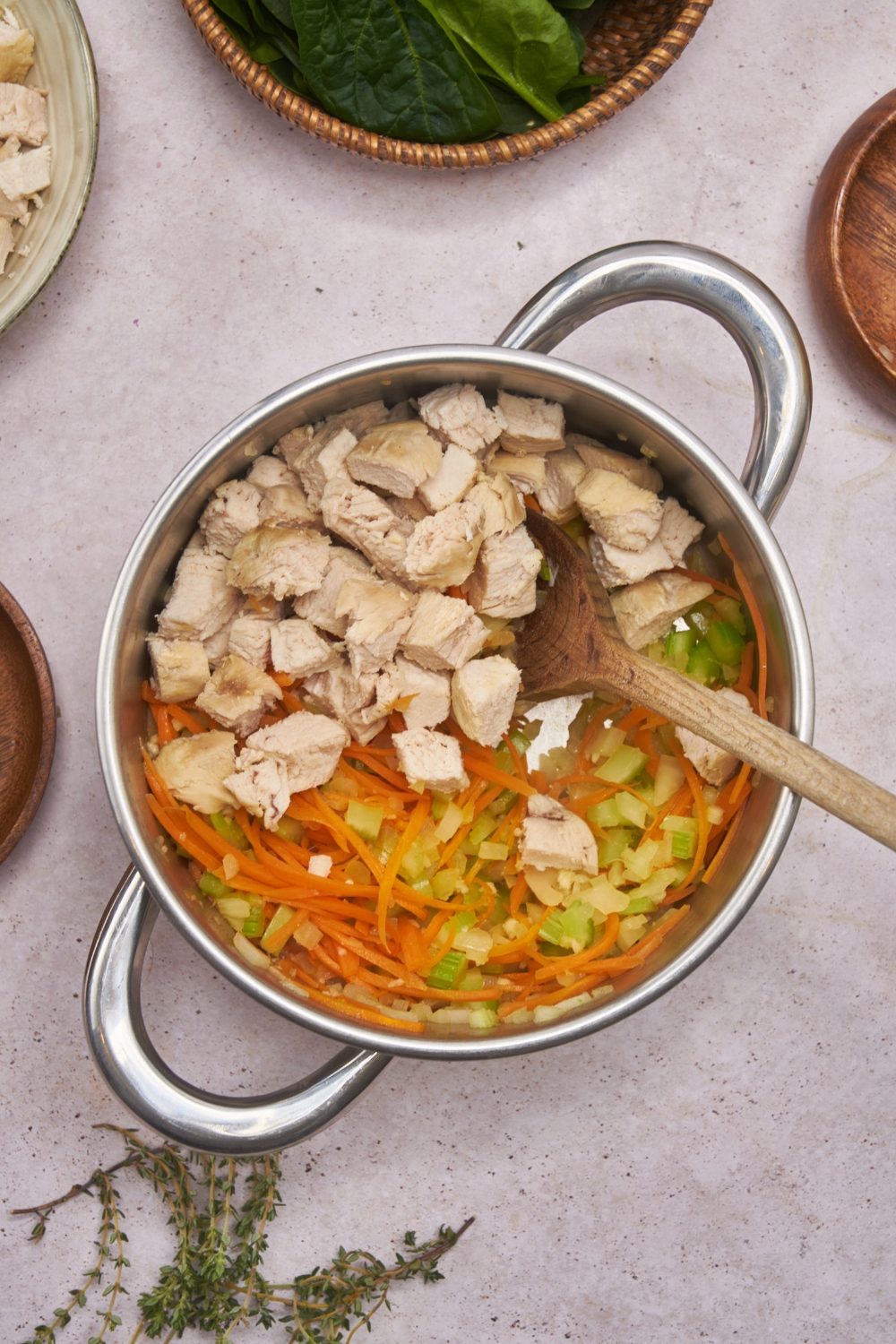 Large pot with diced chicken, shredded carrots, and diced celery simmering in chicken broth.