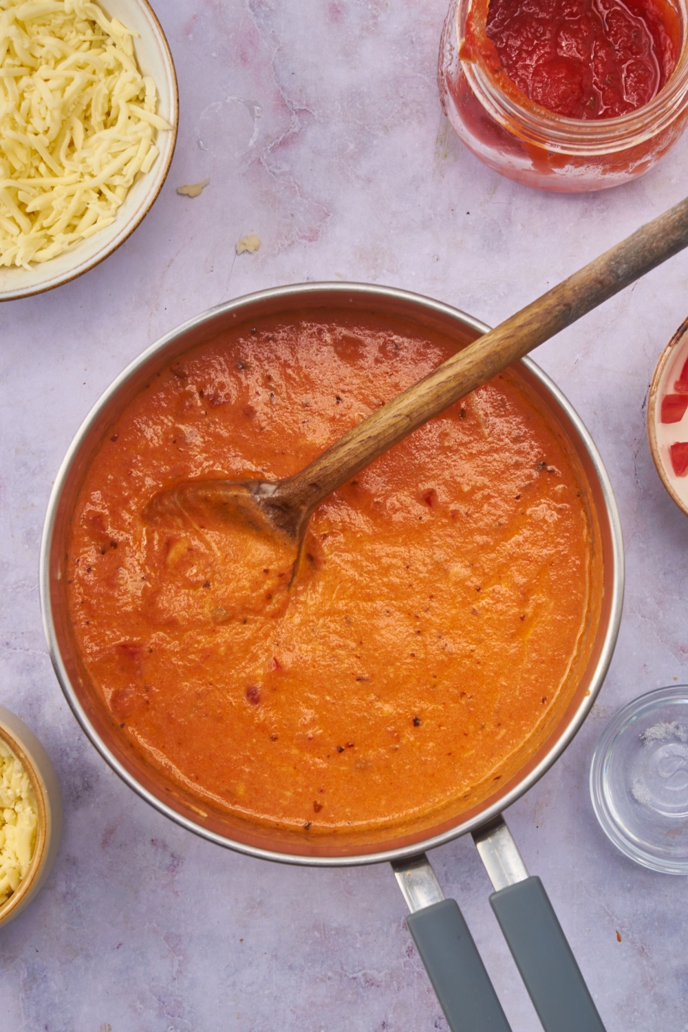 A pot of creamy marinara sauce with a wooden spoon in the pot.