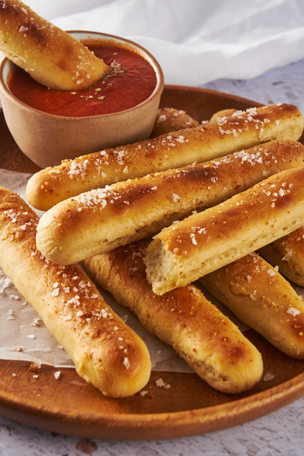 A plate with breadsticks and a small dipping cup of marinara sauce. A breadstick is being dipped into the sauce.