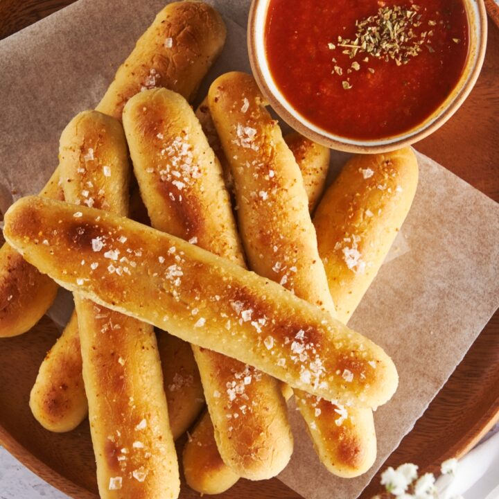 An overhead view of a plate with breadsticks and a small dipping cup of marinara sauce.