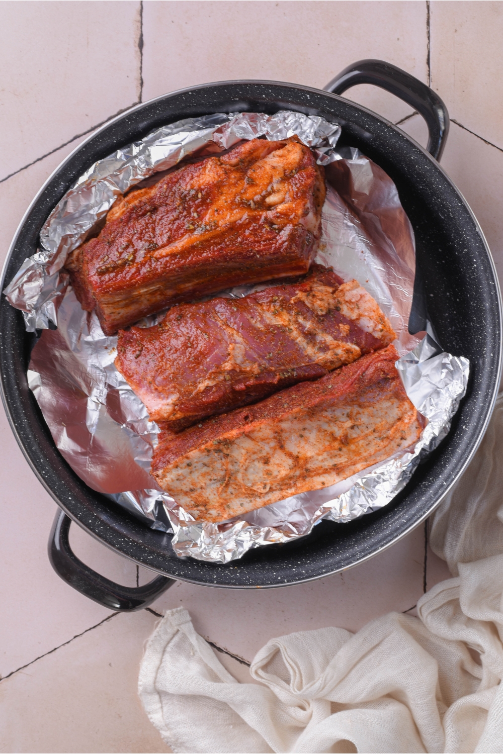 Three seasoned beef ribs in a baking dish and wrapped in aluminum foil.