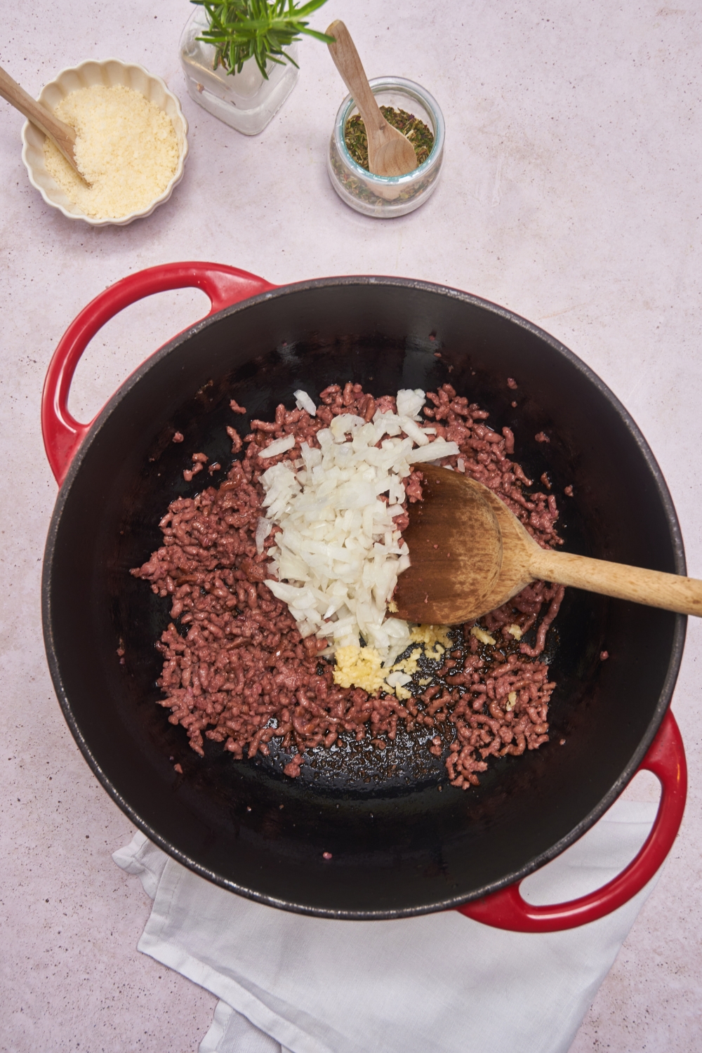 A Dutch oven filled with cooked ground beef and diced onions freshly added to it.