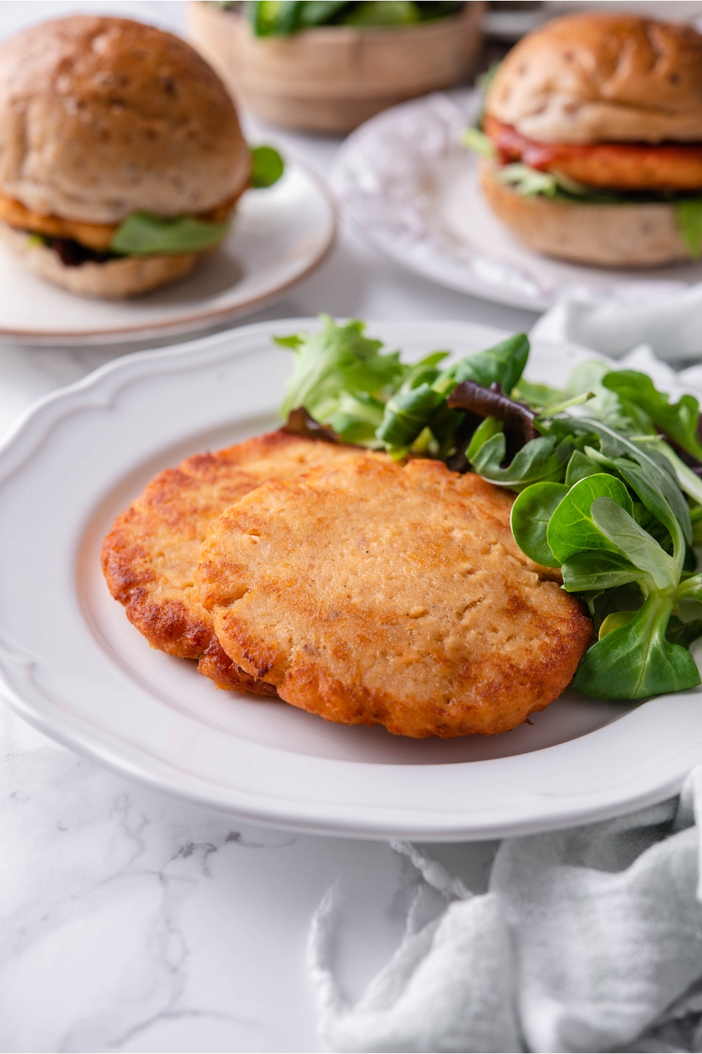Two fried salmon patties layered on top of each other on a white plate with a side salad.