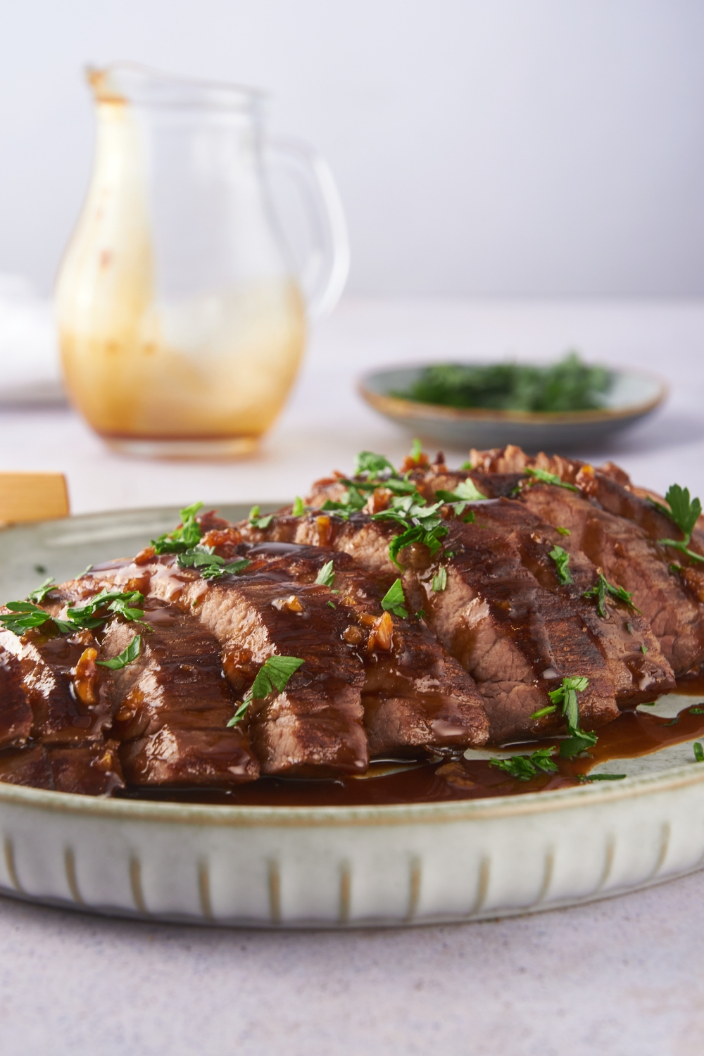 Close up of London broil sliced thin on a plate and covered in a soy sauce glaze and fresh herbs.