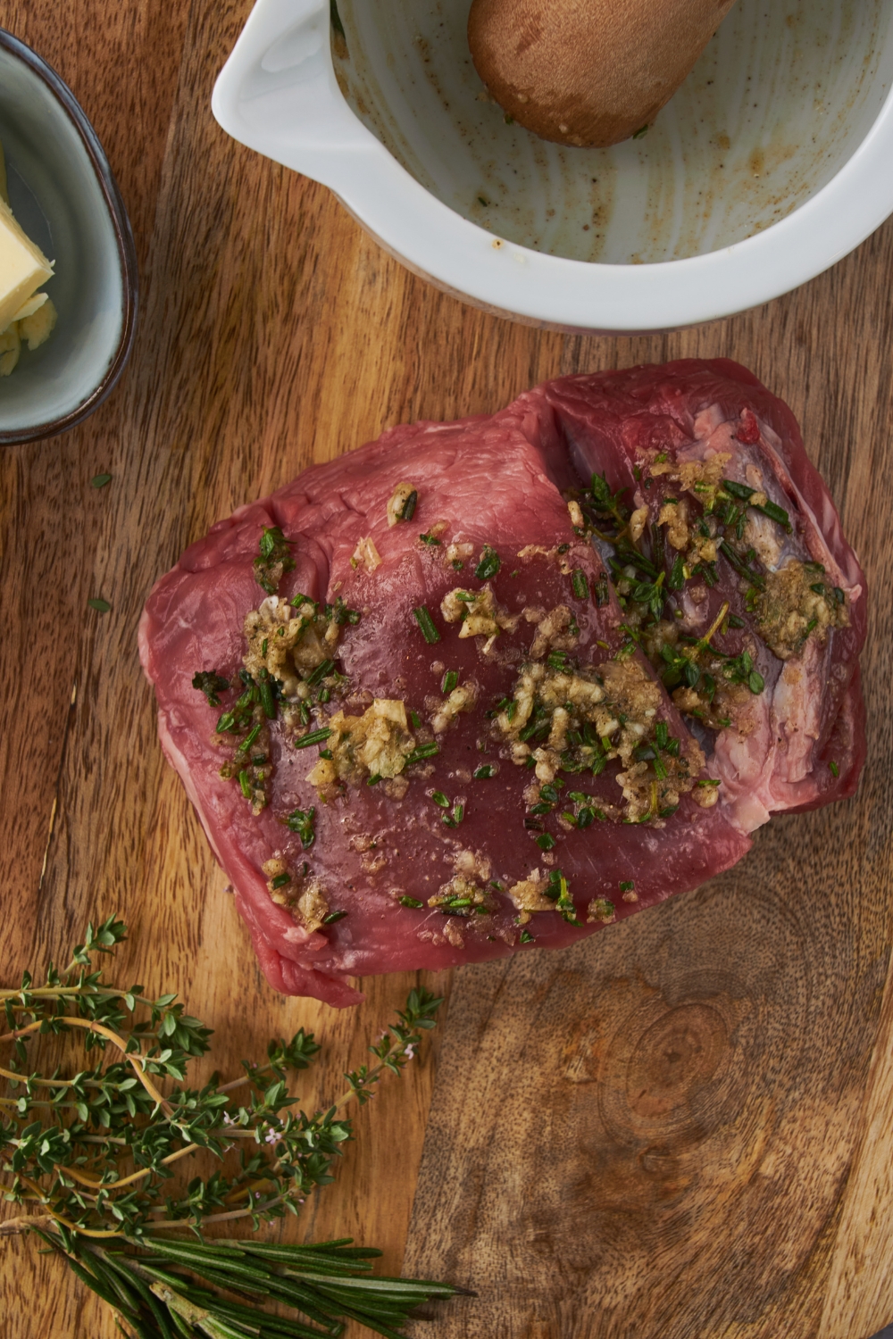 A beef tenderloin seasoned with herbs and garlic on a wooded board.