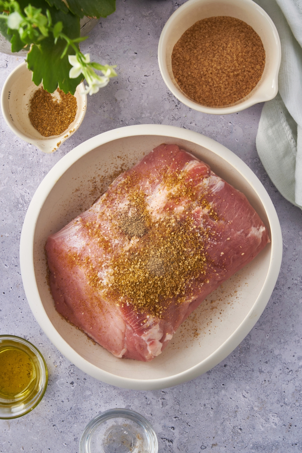 Raw pork shoulder in a bowl covered in a spice rub that has not yet been rubbed into the meat.