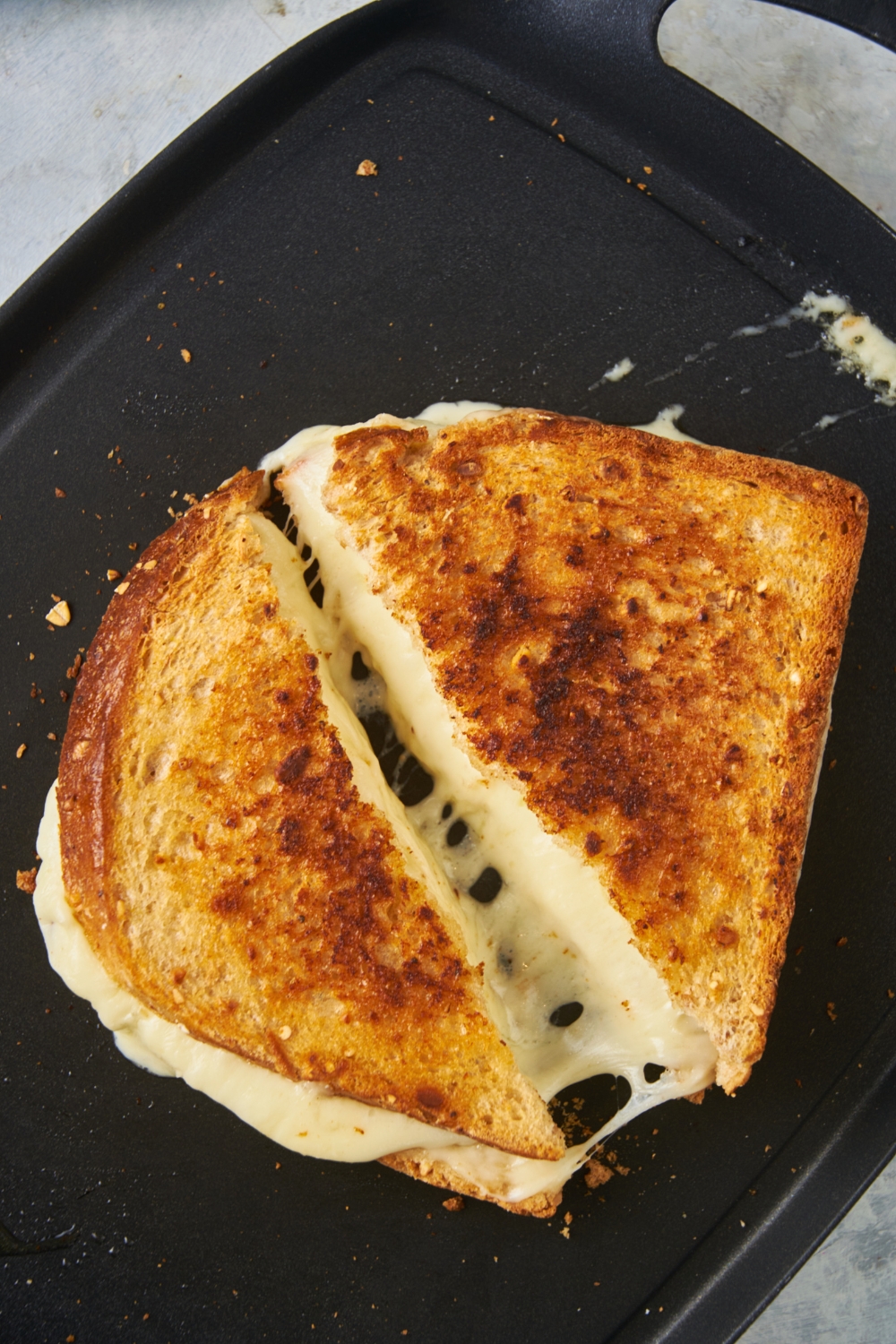 A grilled cheese sandwich on the griddle cut in half with the melty cheese showing.