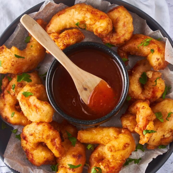 A bunch of beer battered shrimp on a plate surrounding a bowl of sweet and sour sauce.
