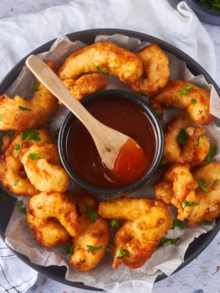 A bunch of beer battered shrimp on a plate surrounding a bowl of sweet and sour sauce.