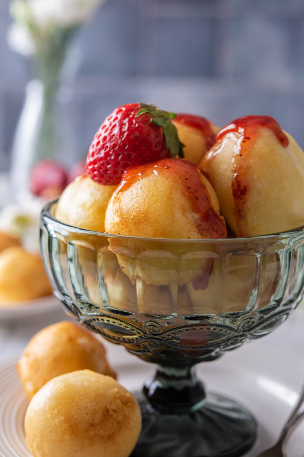 A side view of a dessert bowl with Fried cheesecake balls drizzled in strawberry syrup with a strawberry garnished on top.