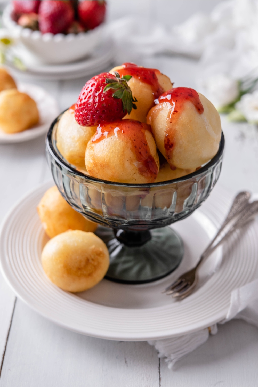 A dessert bowl with Fried cheesecake balls drizzled in strawberry syrup with a strawberry garnished on top.