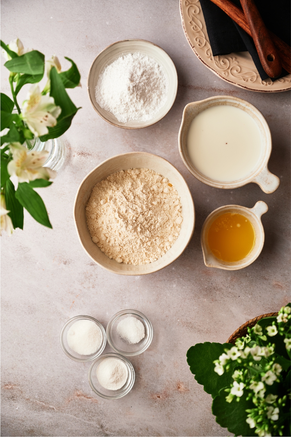 A bowl of flour, a bowl of sugar, a bowl of milk, and a bowl of melted butter.