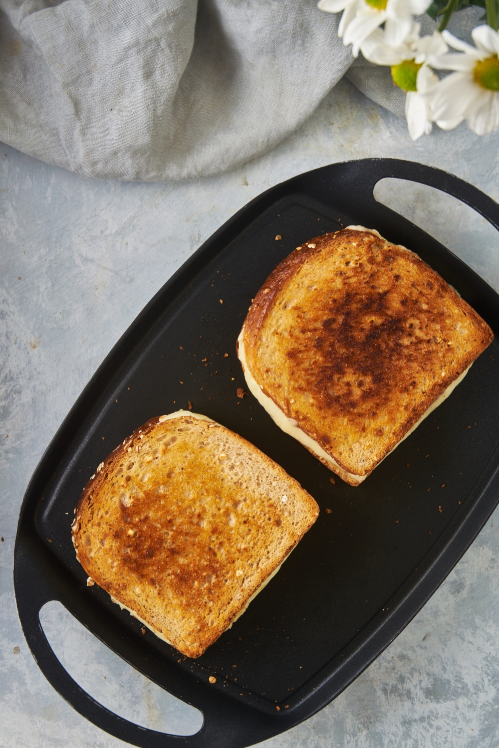 A griddle with two grilled cheese sandwiches being cooked on it. They have just been flipped and the golden brown side is facing up.