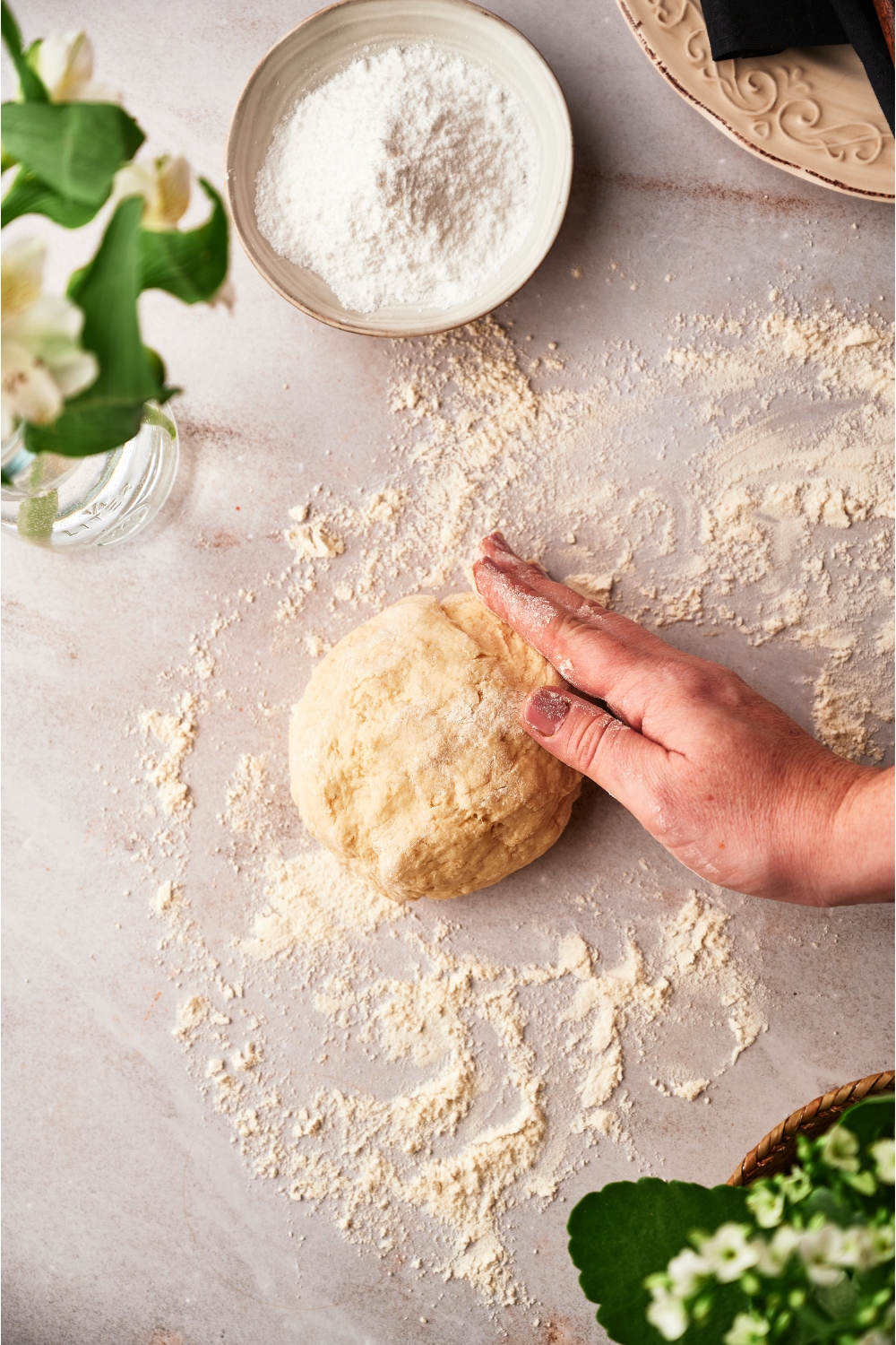 A hand on a ball of dough on top of flour on a table.