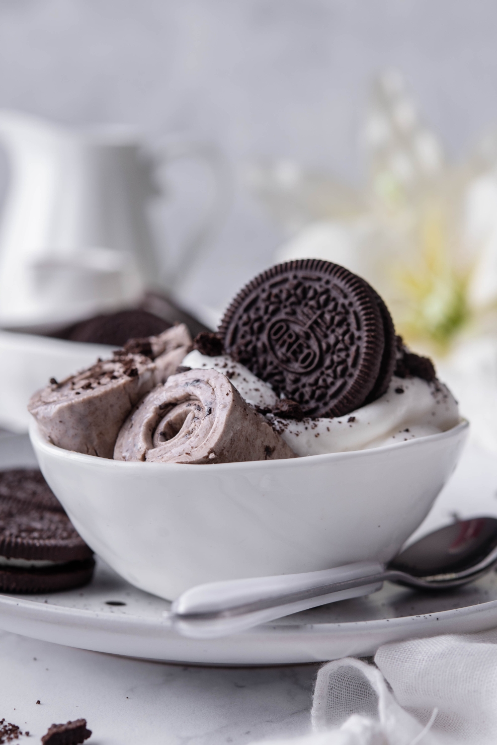 A plate with a bowl with 3 rolled ice creams with whipped cream garnish and a whole oreo.