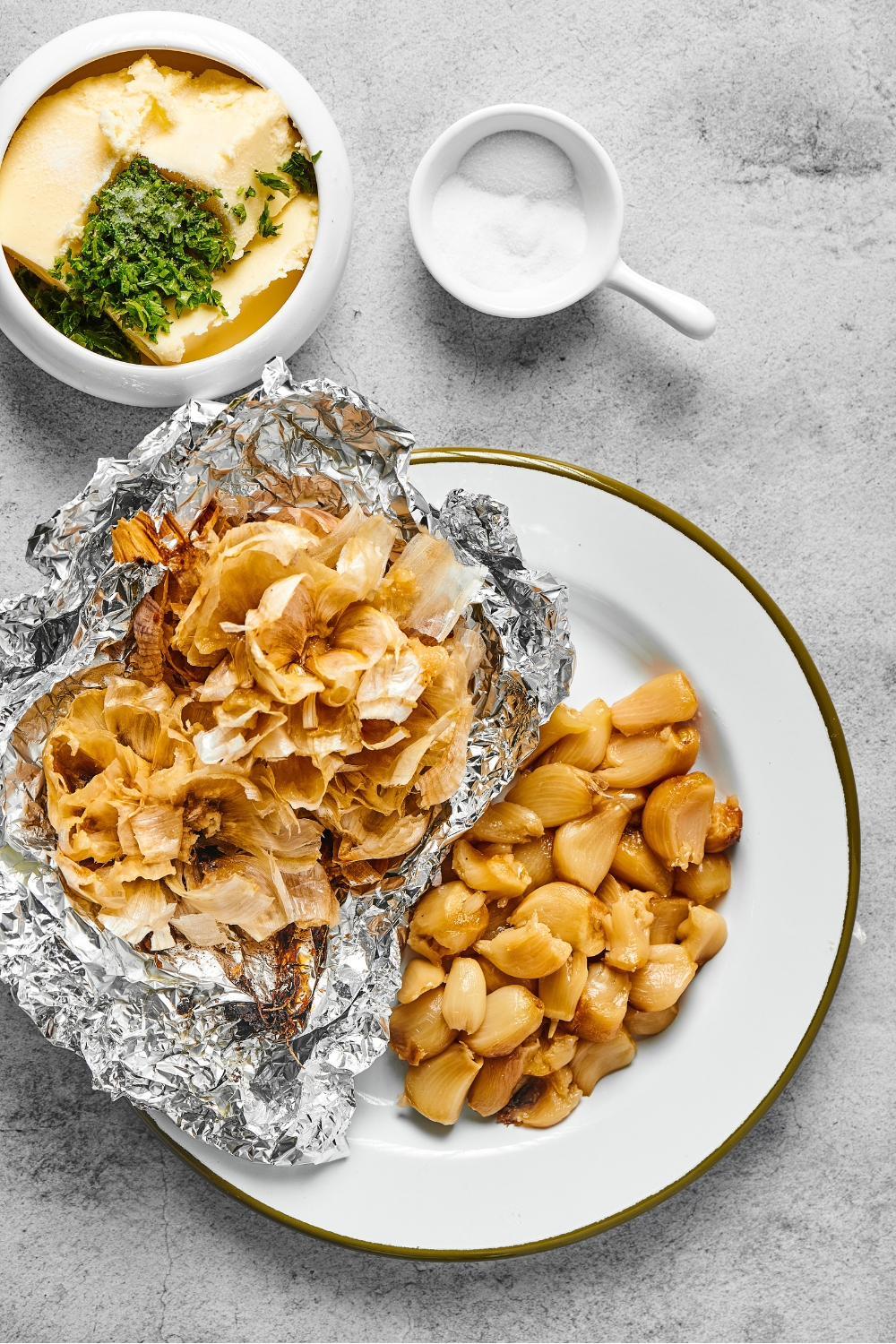 A plate with a bunch of roasted garlic bulbs and aluminum foil with the garlic shells on it.