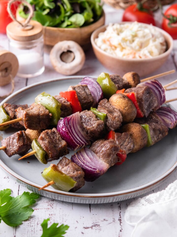 A bunch of beef kabobs with steak, onions, mushrooms, and peppers on skewers.
