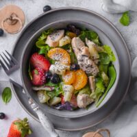 An overhead view of A bowl with panera strawberry poppyseed salad in it served on a saucer with a fork next to it.
