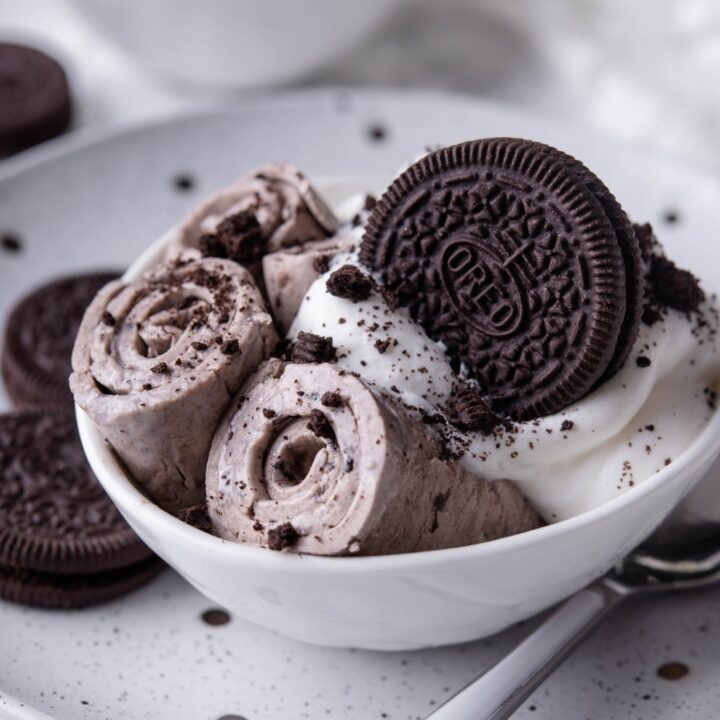 A bowl with 3 rolled up ice creams with whipped cream and a whole oreo on top.