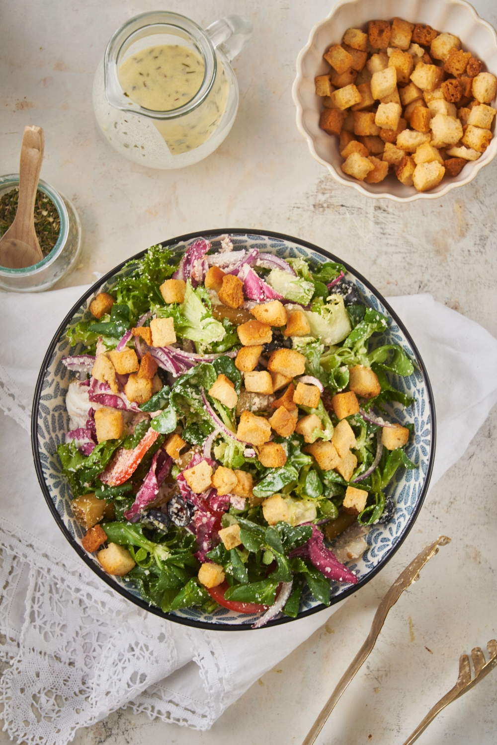 Overhead view of a salad filled with lettuce, peppers, onions, black olives, parmesan cheese, and croutons.