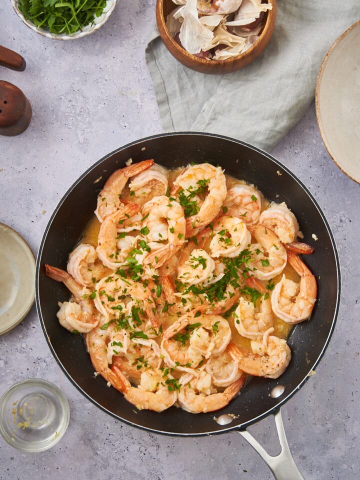 Shrimp scampi in a black skillet and garnished with fresh green herbs.
