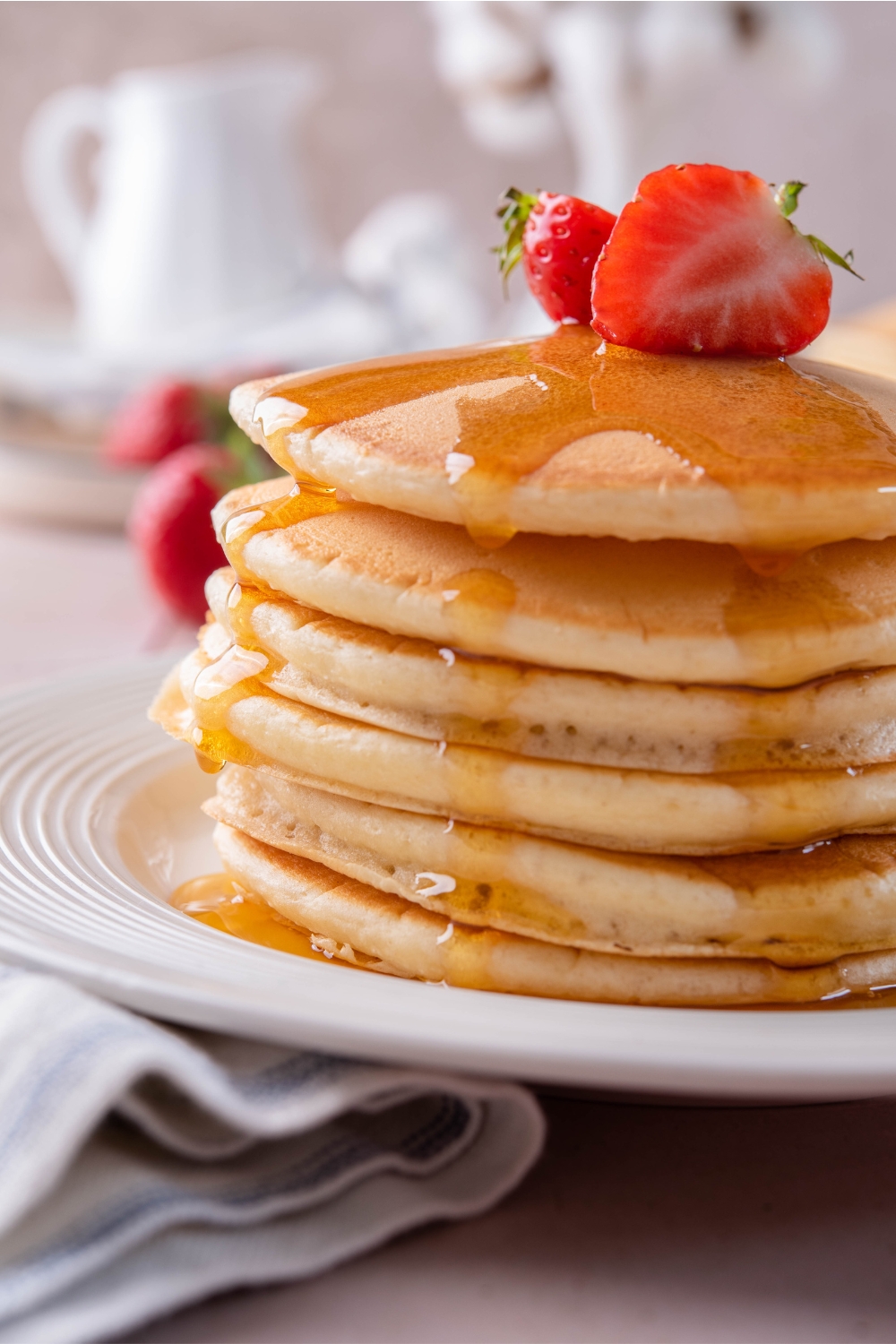 A plate with a stack of pancakes topped with sliced strawberries and fresh maple syrup.
