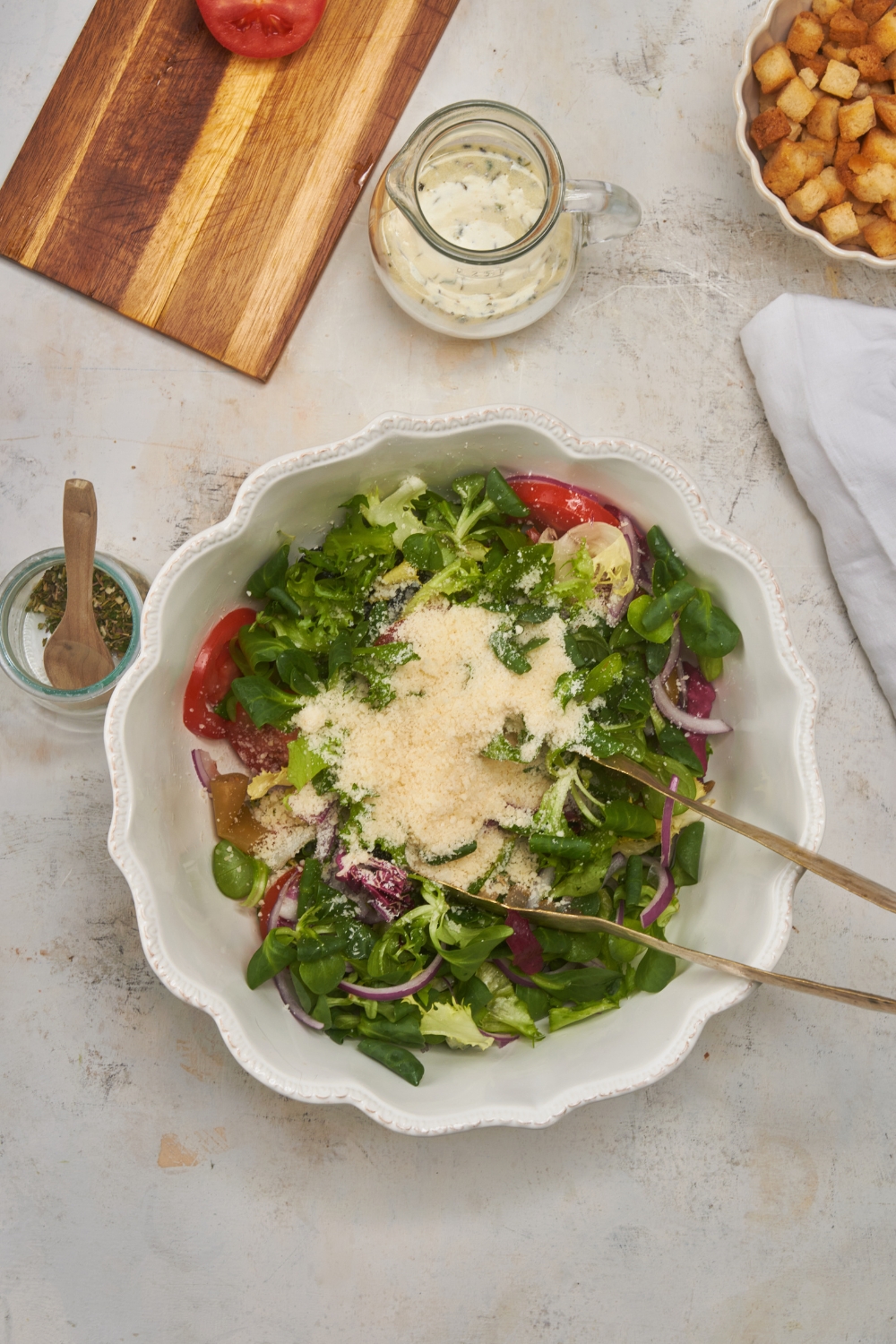 A large white bowl filled with lettuce, tomatoes, onions, grated parmesan cheese and a set of tongs.