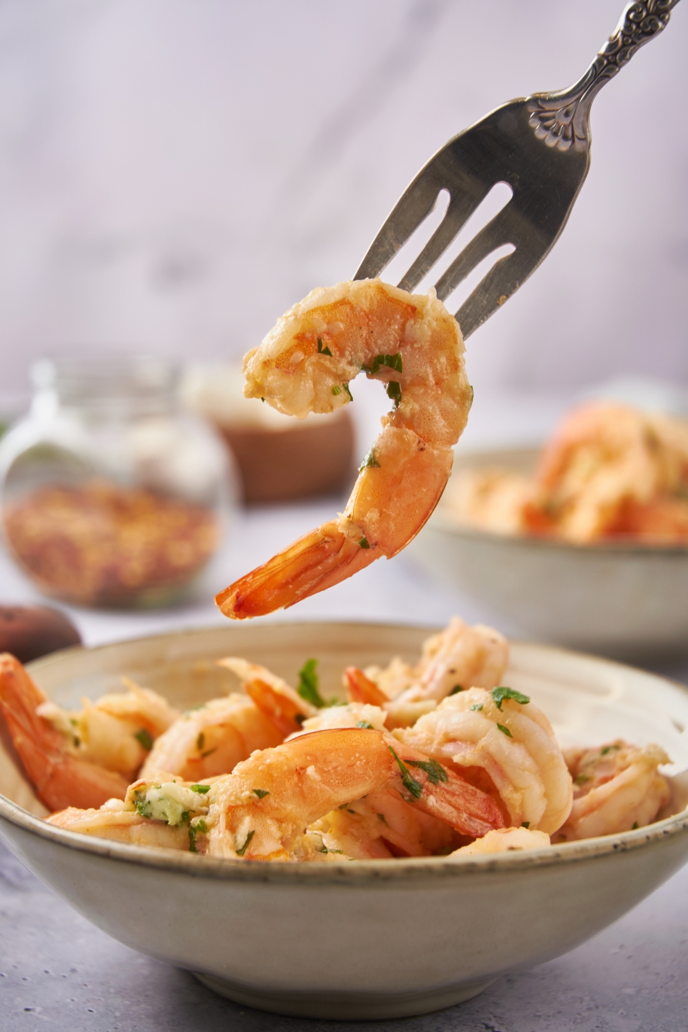 A fork holding a piece of shrimp from a bowl of shrimp scampi.