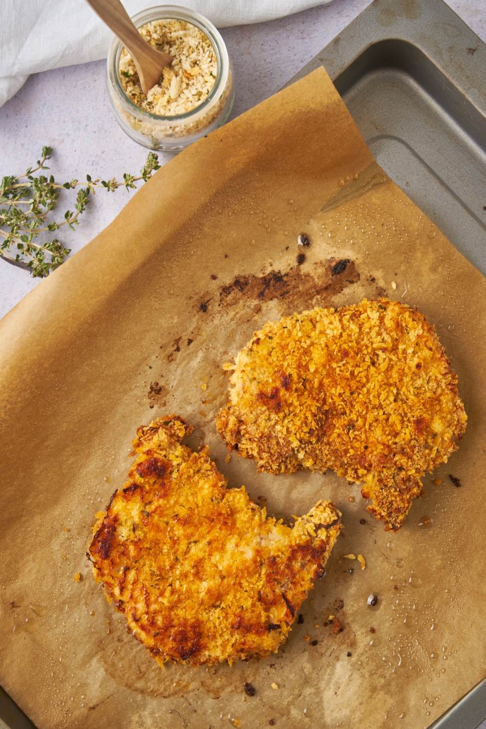 Two golden brown and crispy panko crusted pork chops on a baking sheet lined with parchment paper.