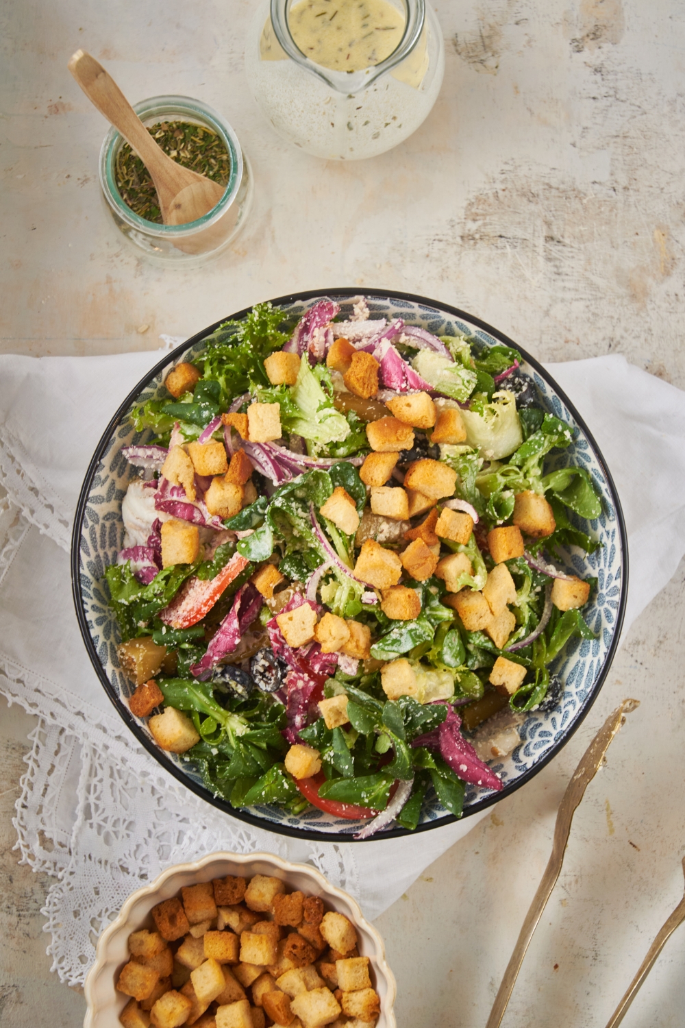 Overhead view of a salad filled with lettuce, peppers, onions, black olives, parmesan cheese, and croutons.