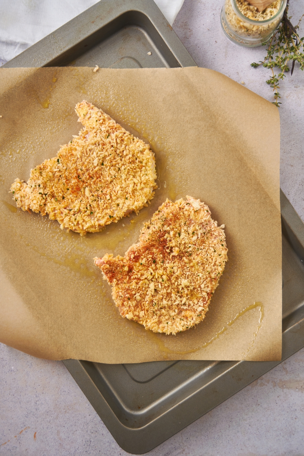 Two raw pork chops coated in a panko breading on a baking sheet lined with parchment paper.
