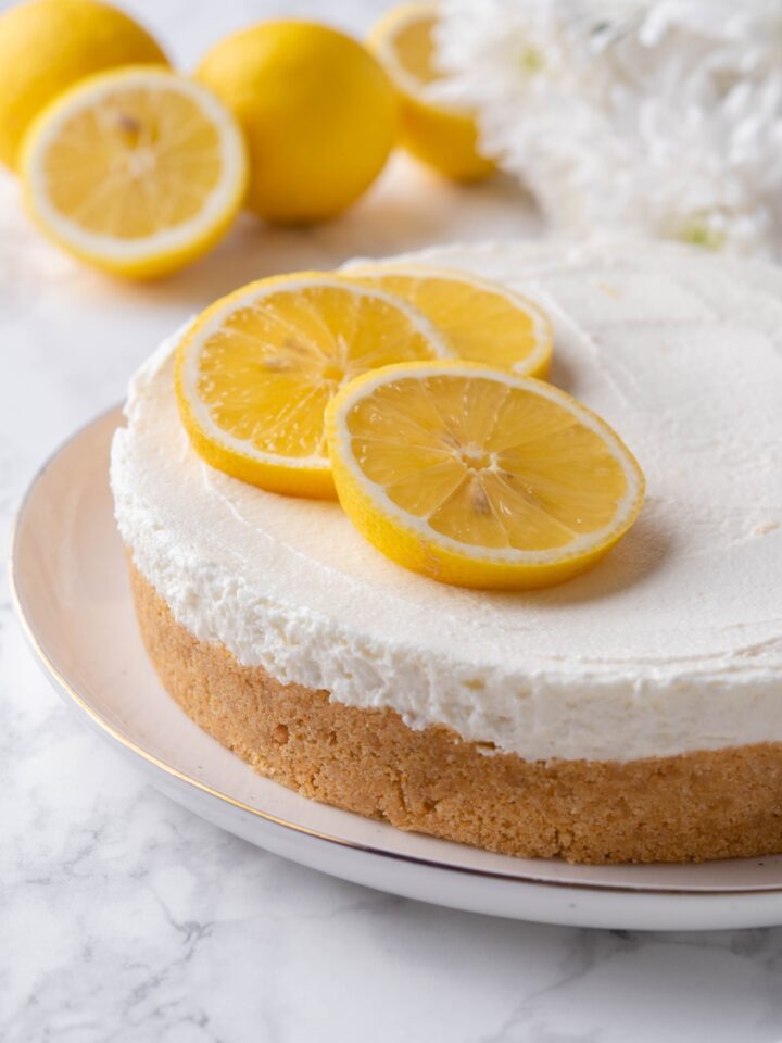 A close up of a whole cheesecake on a serving plate garnished with slices of lemon.