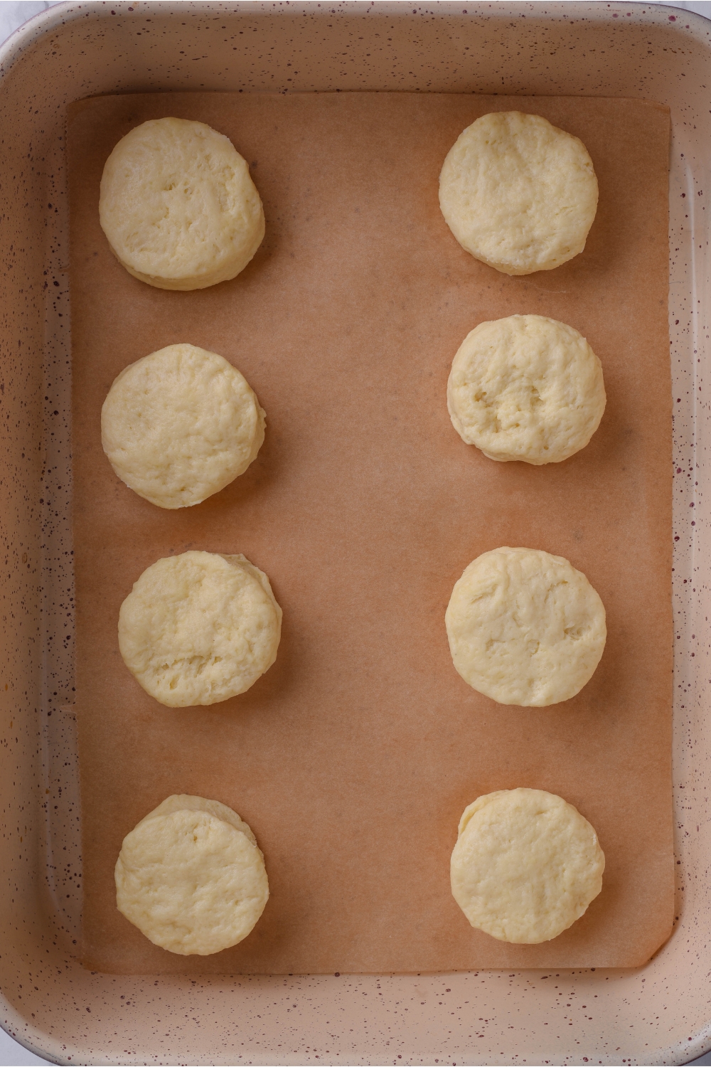 A baking sheet lined with parchment paper with 8 cutout biscuits
