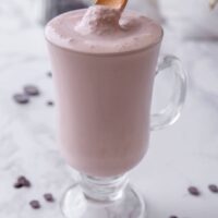 A glass filled with a Wendy's chocolate frosty with a wooden spoon placing some of the frosty on top.