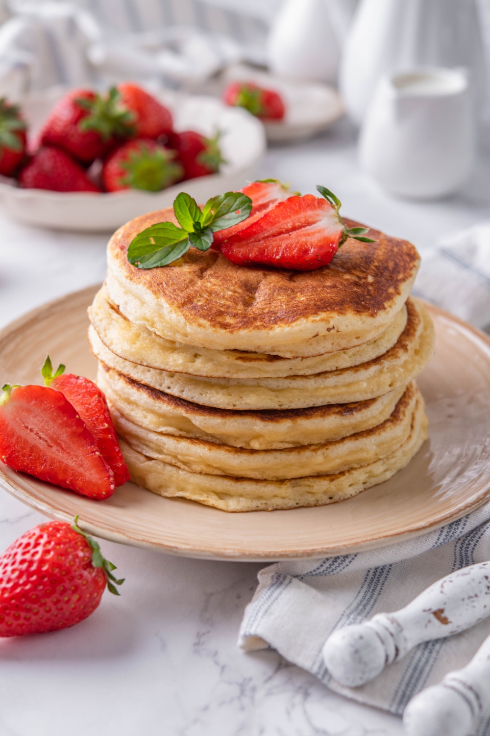 A plate with a stack of pancakes topped with sliced strawberries and a garnish of mint.