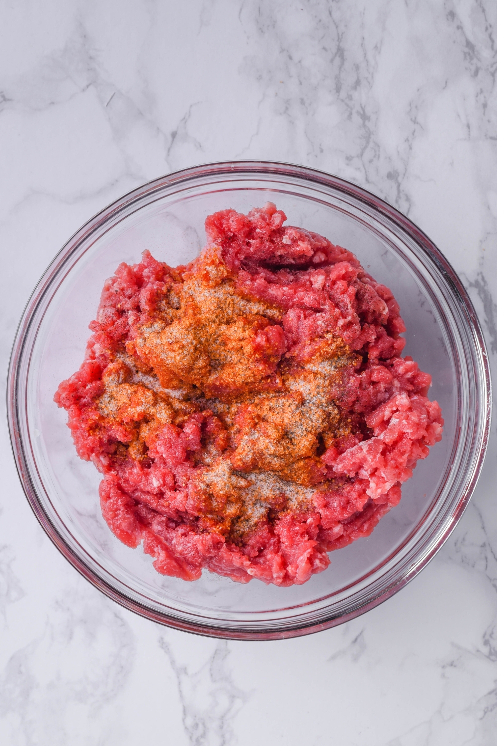 A mixing bowl with lean ground beef and old bay seasonings.