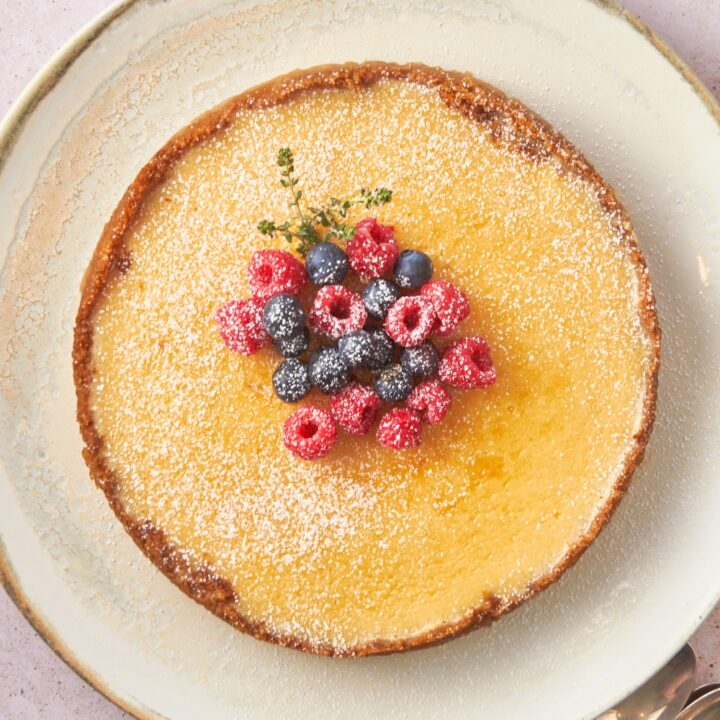 Fresh berries on top of a classic Philadelphia cheesecake on a white plate on a counter.