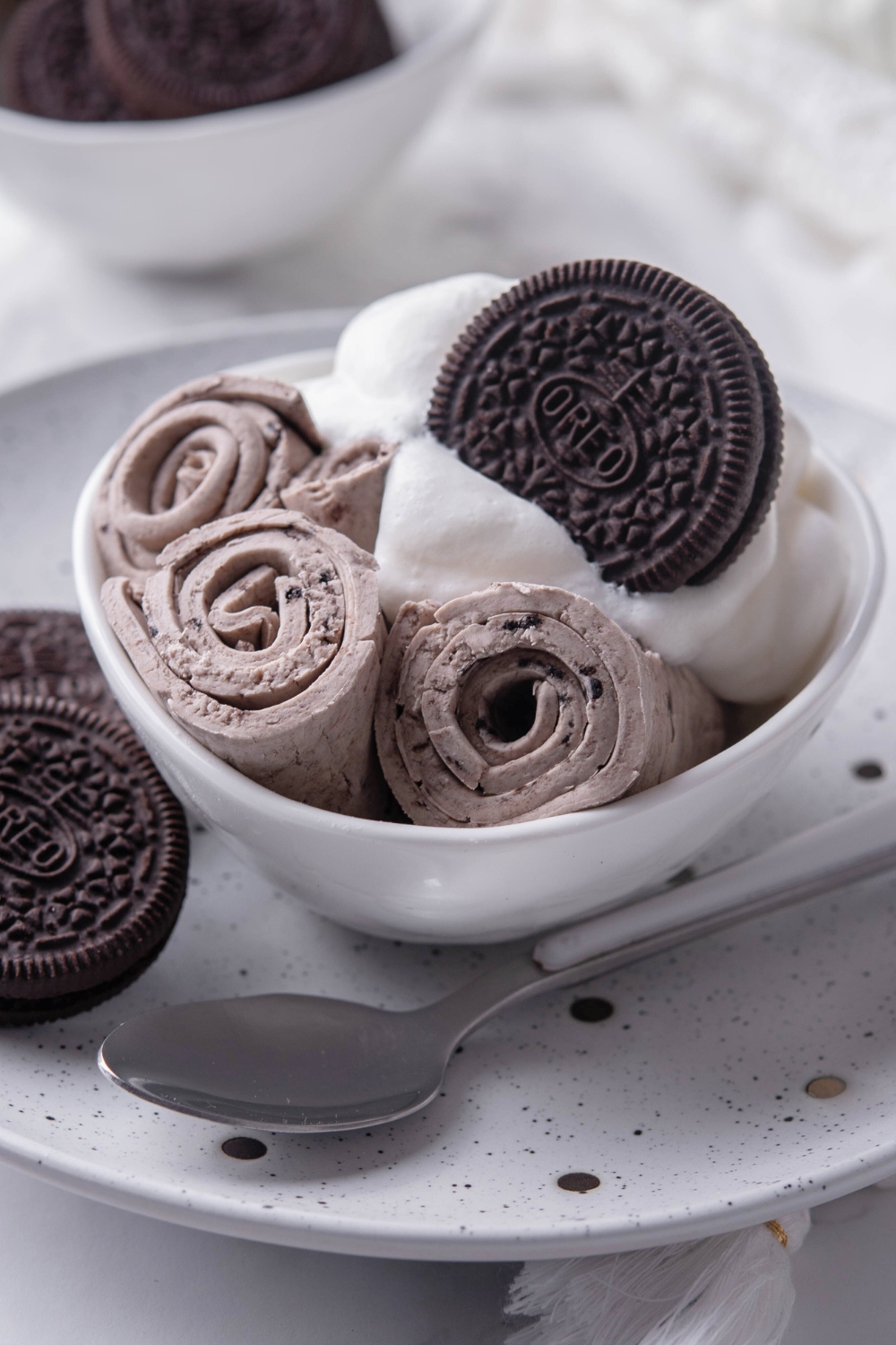 Three ice cream rolls against one another in a bowl with whipped cream and an Oreo on the side of the one bowl.